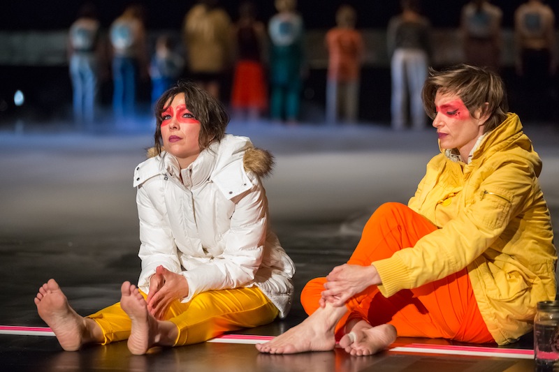 Emily Johnson and Krista Langberg sit onstage in brightly colored parks with red warrior paint on their faces 
